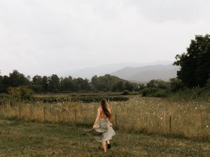 a girl in a dress runs towards a field with the blue ridge mountains high in the background in Western North Carolina near Asheville