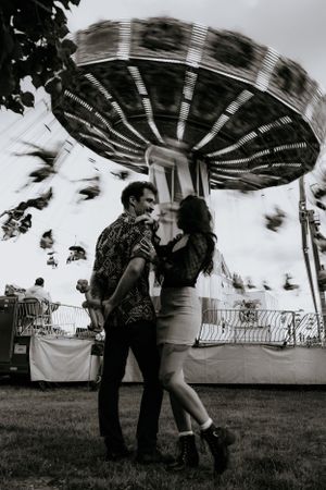 a monochrome photo of a couple standing in front of the moving swings ride at the carnival in Western North Carolina near Asheville