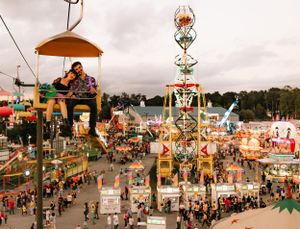 a couple leans on one another in a colorful landscape of the carnival as they are high above in the chair lift