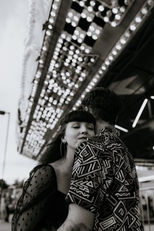 a monochrome photo of a couple standing in front of the lights of the carnival rides in Western North Carolina near Asheville