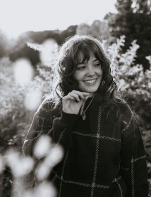 in black and white girl in a sweater chews on a wheat grass surrounded by golden light and flowers in Western North Carolina near Asheville
