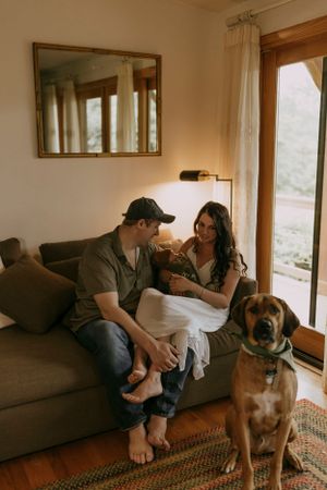 a mother, father, their infant son, and a dog sit inside on the couch together