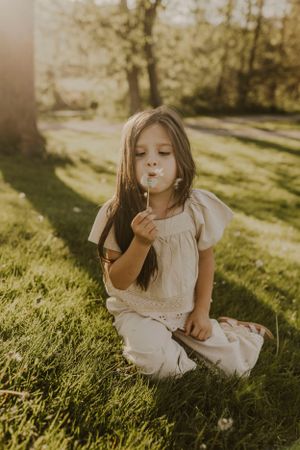 a young girl blows the seeds of a dandelion