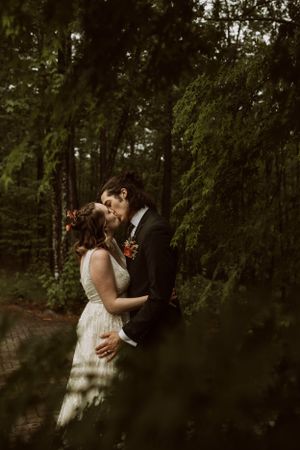 a bride and groom share a kiss framed by an evergreen tree