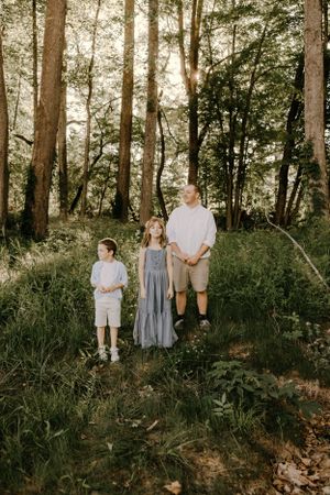 a father stands with his two children in the forest
