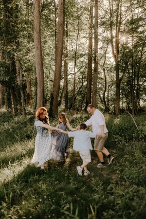 a family of 4 hold hands and play in a circle in the forest