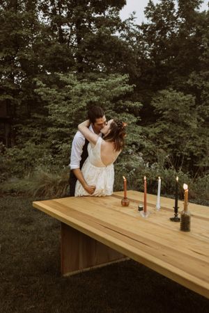 a bride and groom lean on a table filled with candles to share a kiss outdoors in nature in the mountains of Asheville