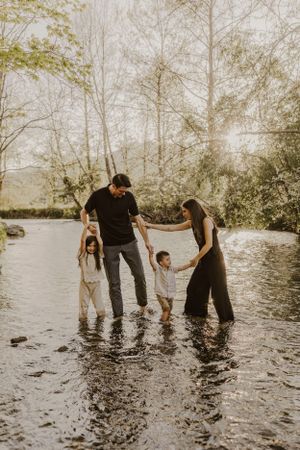 a family plays in the creek together as light bursts through the trees