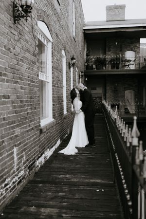 a couple stand on a wooden walkway by a brick building in black and white in Western North Carolina near Asheville