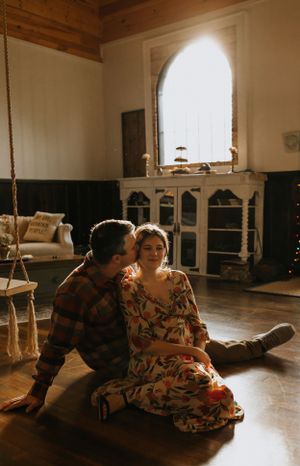 a man kisses a woman on the cheek as they sit on the floor in front of a window that is flooded with light