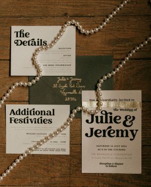 wedding invites on a wooden backdrop with a long string of pearls across the frame