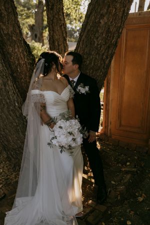 a bride and groom share a kiss by the tree