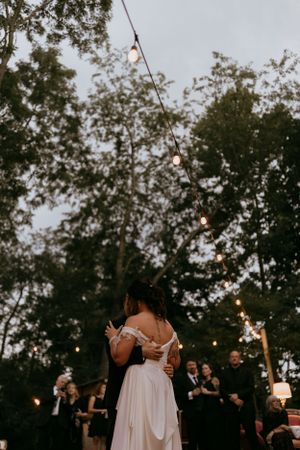 a bride and groom share a first dance surrounded by trees and their wedding guests
