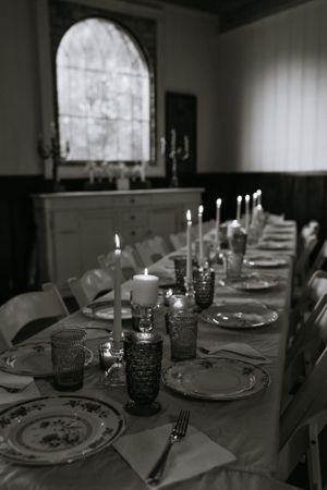 a monochrome table set with lit candles in front of an arched window that is letting light in
