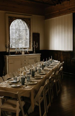 a long table set with plates cups and lit candles in front of an arched window that is letting light in
