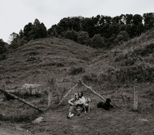 a couple and their dogs sit near a fence with a large hill behind them in black and white in Western North Carolina near Asheville