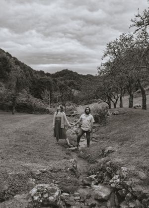 a black and white photo of a couple straddling a creek with the mountains in the back in Western North Carolina near Asheville