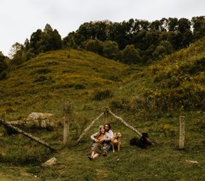 a couple and their dogs sit near a fence with a large hill behind them in Western North Carolina near Asheville and Boone