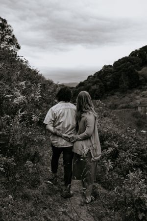 in black and white a couple holds their hands together behind their backs on a trail  in Western North Carolina near Asheville
