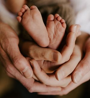 two sets of hands cradle the tiny feet of an infant baby