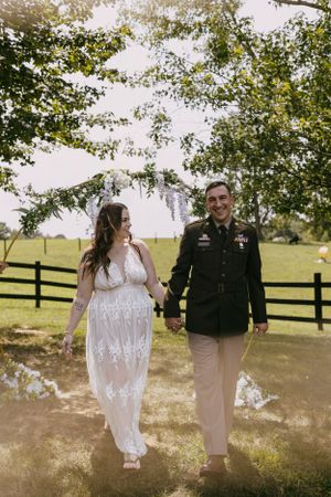 an army man and his wife walk away from their flower arch wedding alter with a fence in the background