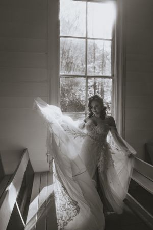 a monochrome shot of a bride throwing her dress in the air in front of the window of Cataloochee Valley Chapel as the light pours in