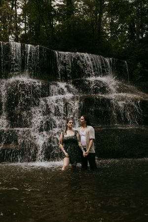 a couple stand fiercely in the water in front of a waterfall