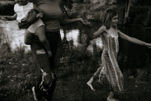 a black and white photo of a mom holding a toddler and being led along by her child by the creek in Western North Carolina in Waynesville