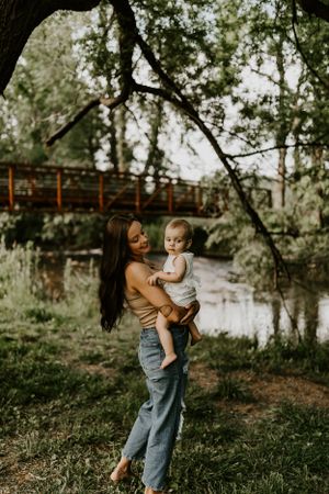 a mother holds her toddler under a tree by the creek in Western North Carolina just outside of Asheville and Waynesville