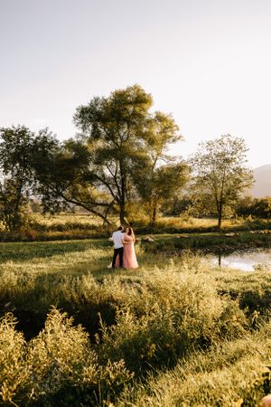 a couple stand between two ponds as the sun is setting over the Blueridge mountains in Western North Carolina near Asheville