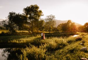 a couple stand between two ponds as the sun is setting over the Blueridge mountains in Western North Carolina near Asheville