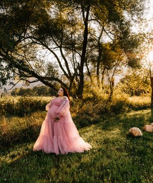 a woman in a pink dress poses under a tree that is illuminated in golden light in Western North Carolina near Asheville