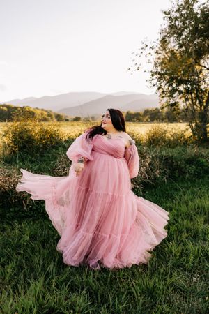 a woman in a pink dress twirls in a field with the Blueridge mountains in the background in Western North Carolina near Asheville