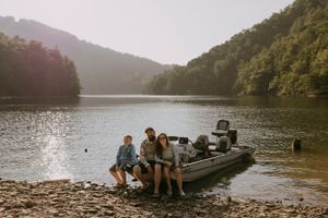 a family of three sit on their boat on an island on the lake that is surrounded by mountains