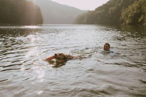 a young boy and his dog swim in the lake as the light bounces off the water