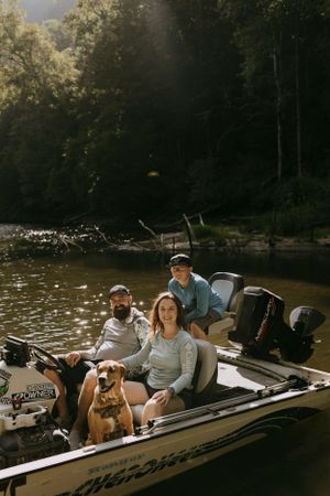 a family and their dog sit in their boat on the lake with the water glistening behind them
