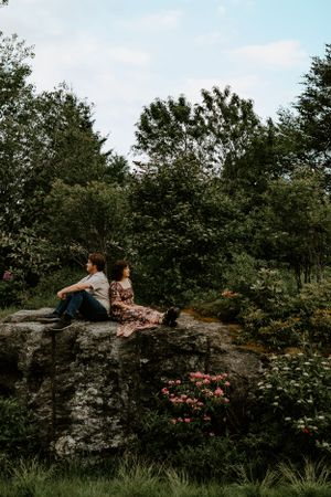 A couple leans on one another on top of a rock surrounded by flowers on the Blue Ridge Parkway in Western North Carolina near Asheville