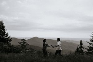 a couple with outstretched hands play lovingly on the blue ridge parkway in Western North Carolina just outside of Asheville with mountains