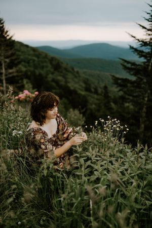 a girl picks flowers with the blue ridge mountains in the background on the Blue Ridge Parkway in Western North Carolina near Asheville
