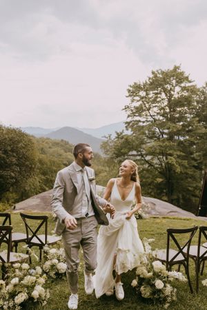 a bride and groom joyfully bound down the aisle filled with white flowers leaving the blue ridge mountains in the distance