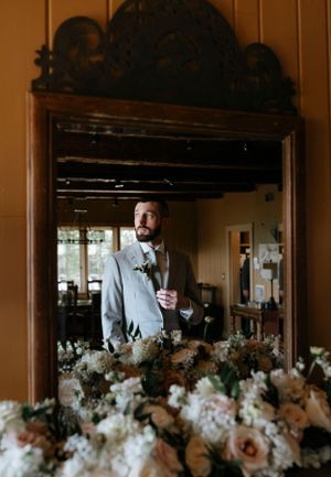 a groom seen in the mirror with white flowers in front of him