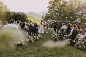 a bride and groom say their vows in front of their wedding guests with the blue ridge mountains in the distance