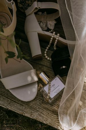 details of a brides shoes, jewelry, veil, and perfume sitting on a wooden background