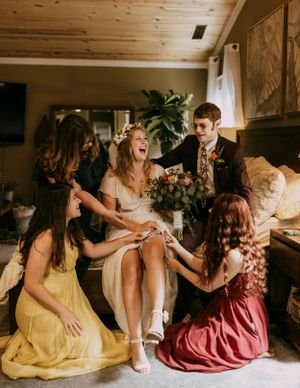 a bride celebrates with her closest friends sitting on a bed and laughing