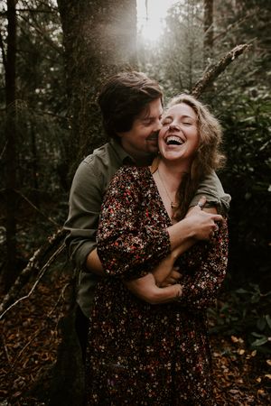 couple snuggled under a tree with golden light coming in from behind them in the mountains of asheville western north carolina