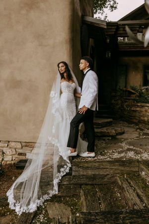 a bride and groom stand leaning on a stucco wall