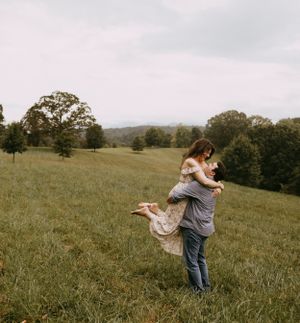 a man picks up a woman in a dress and spins her around in a field overlooking the Blueridge Mountains on the Biltmore estate in Asheville