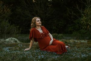 a mother to be sits among the blue flowers on the blue ridge parkway in in Western North Carolina just outside of Asheville