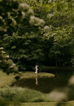 a couple embrace after their wedding on the peninsula of a pond framed by flowers and shrubbery