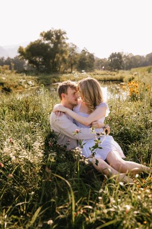 a couple hug in a field with a pond and flowers in the mountains of Western North Carolina near Asheville